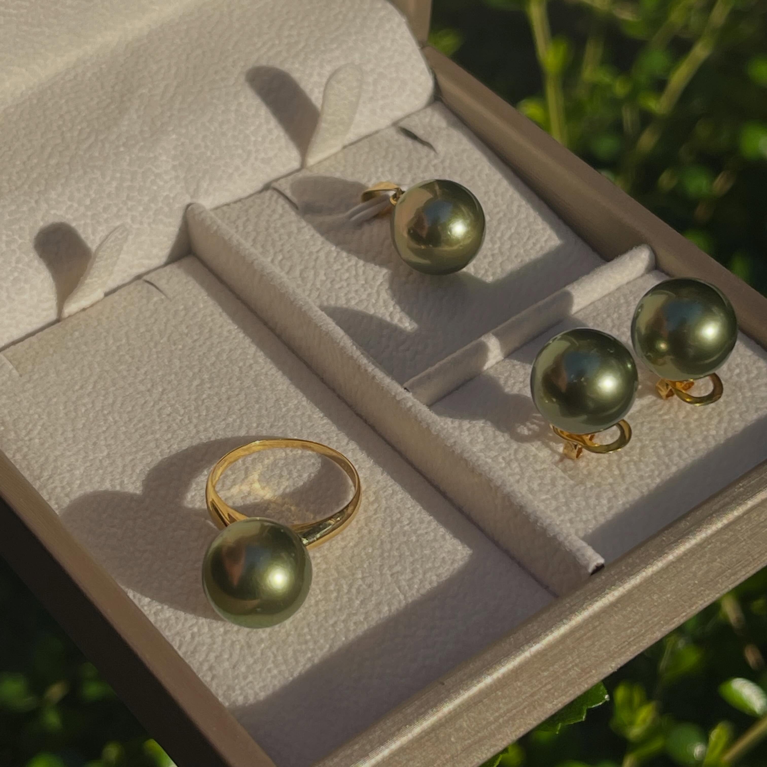 13mm pistachio green South Sea pearl ring and earrings set in 14K gold displayed in a jewelry box under natural light.