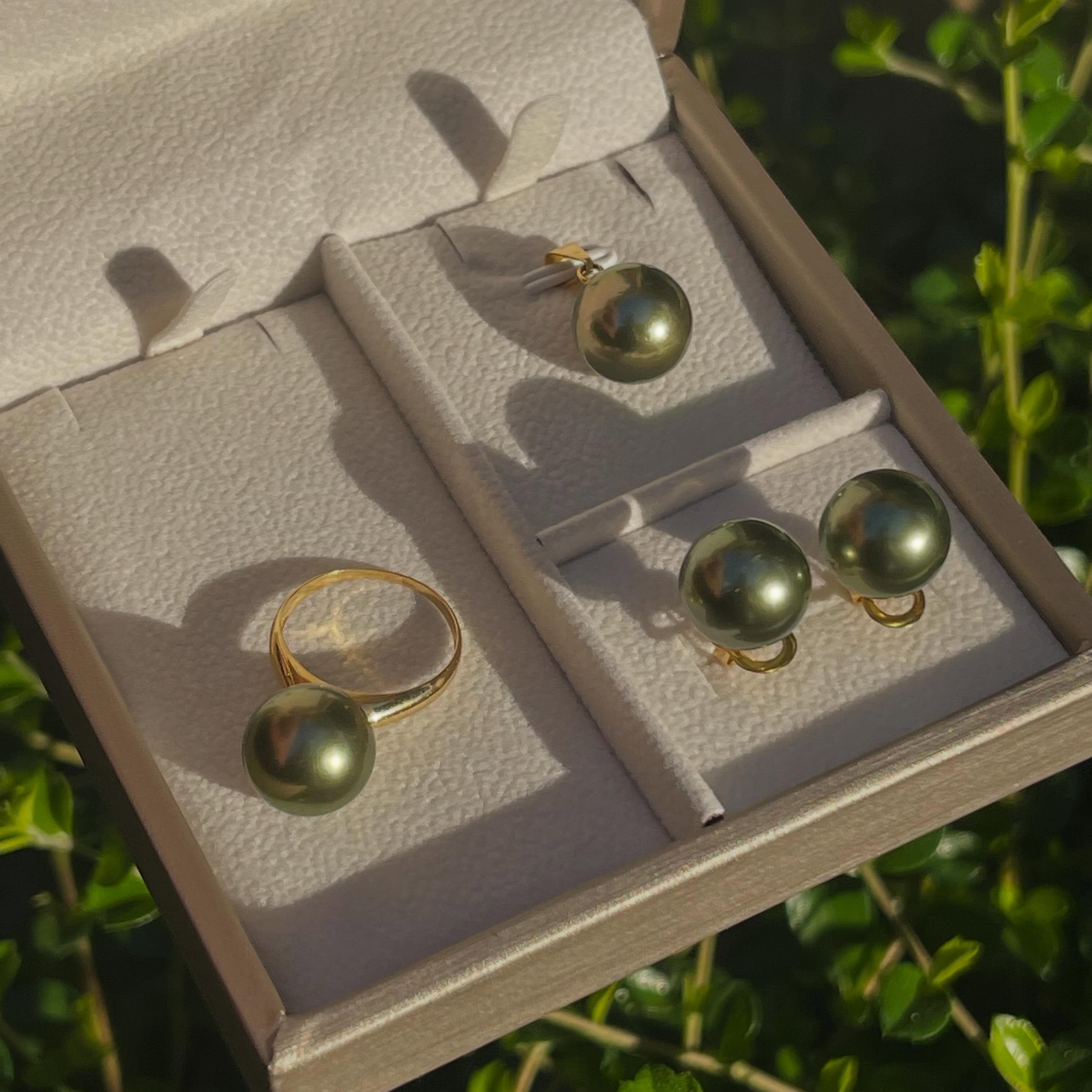 13mm pistachio green South Sea pearl ring and earrings set in 14K gold displayed in a jewelry box under natural light.
