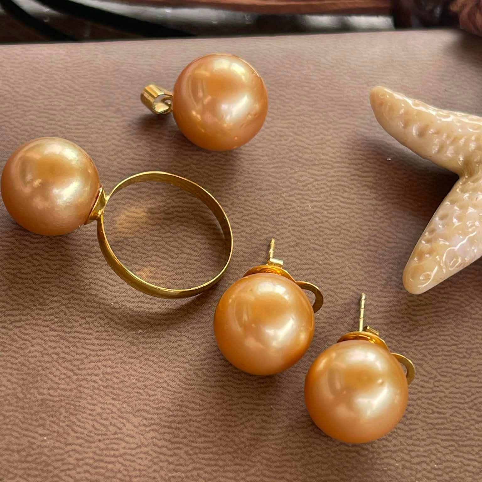 Gold hoop earrings with large brown pearls on a textured surface with a starfish.