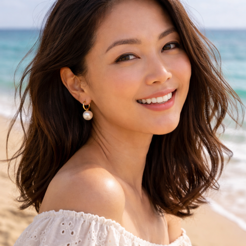 woman wearing white hoop earrings in gold setting in a beach.