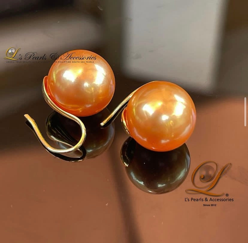 A pair of golden South Sea pearl spoon earrings set in 14k gold, displayed against a reflective background.
